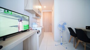 A modern kitchen with a TV displaying a golf game, a white sink, and a fan. - Strategic And Homey 1Br At The City Square Apartment (Surabaya)