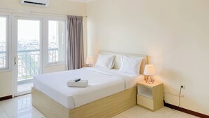 A hotel room with a bed, bedside lamps, a window with curtains, and an air conditioning unit. - Comfort Studio (No Kitchen) Grand Palace Kemayoran Apartment (Free Ipl & Utilities) (Jakarta)