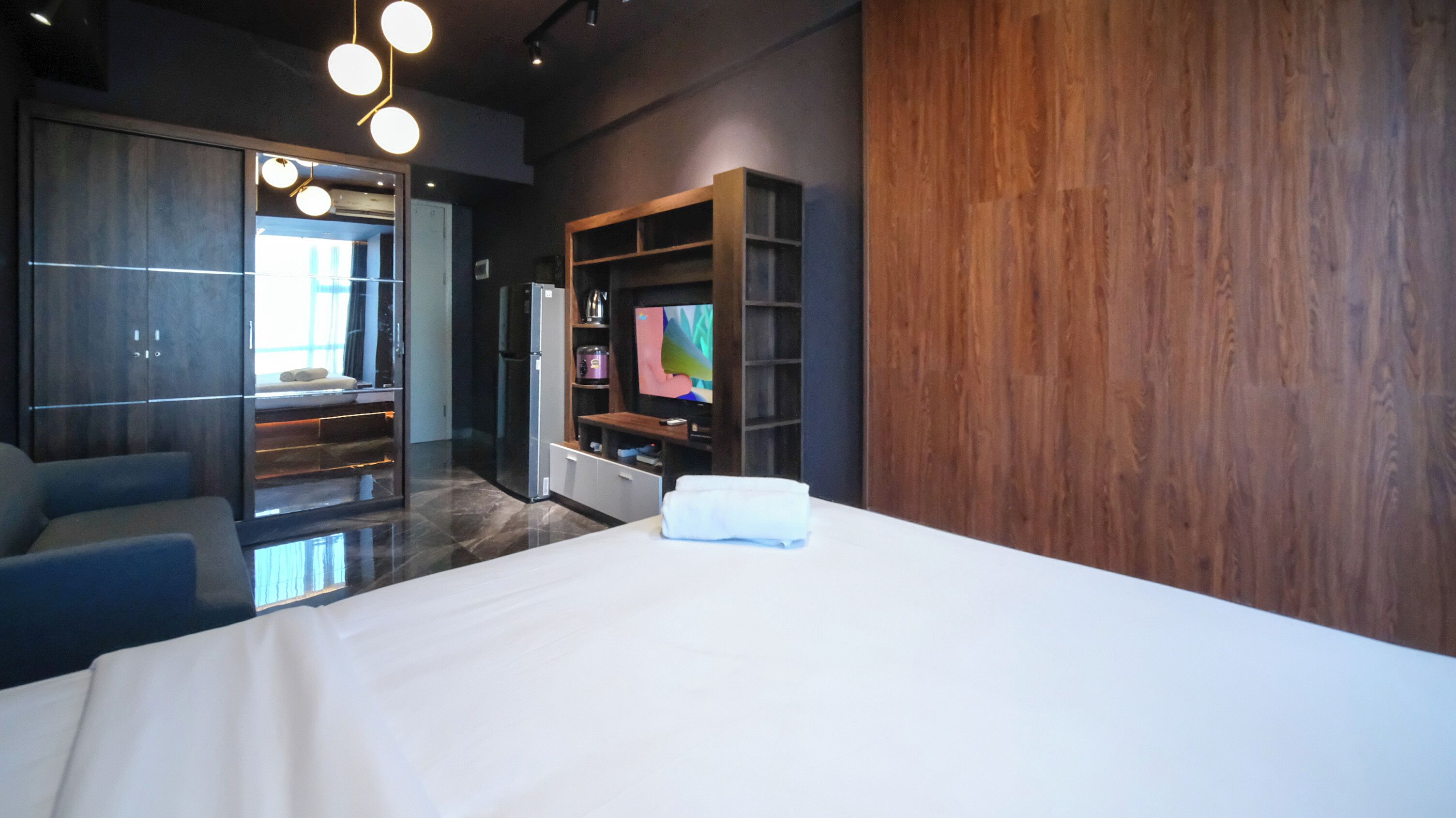 Une chambre d’hôtel moderne dotée d’un grand lit, d’une télévision, d’une armoire en bois et d’un coin salon avec un canapé et des fauteuils.