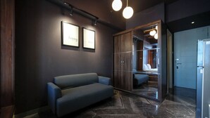 A modern hotel lobby with a dark wall, a blue sofa, and a mirror reflecting a bedroom. - Simple And Modern Studio (No Kitchen) Anderson Supermall Mansion Apartment (Surabaya)