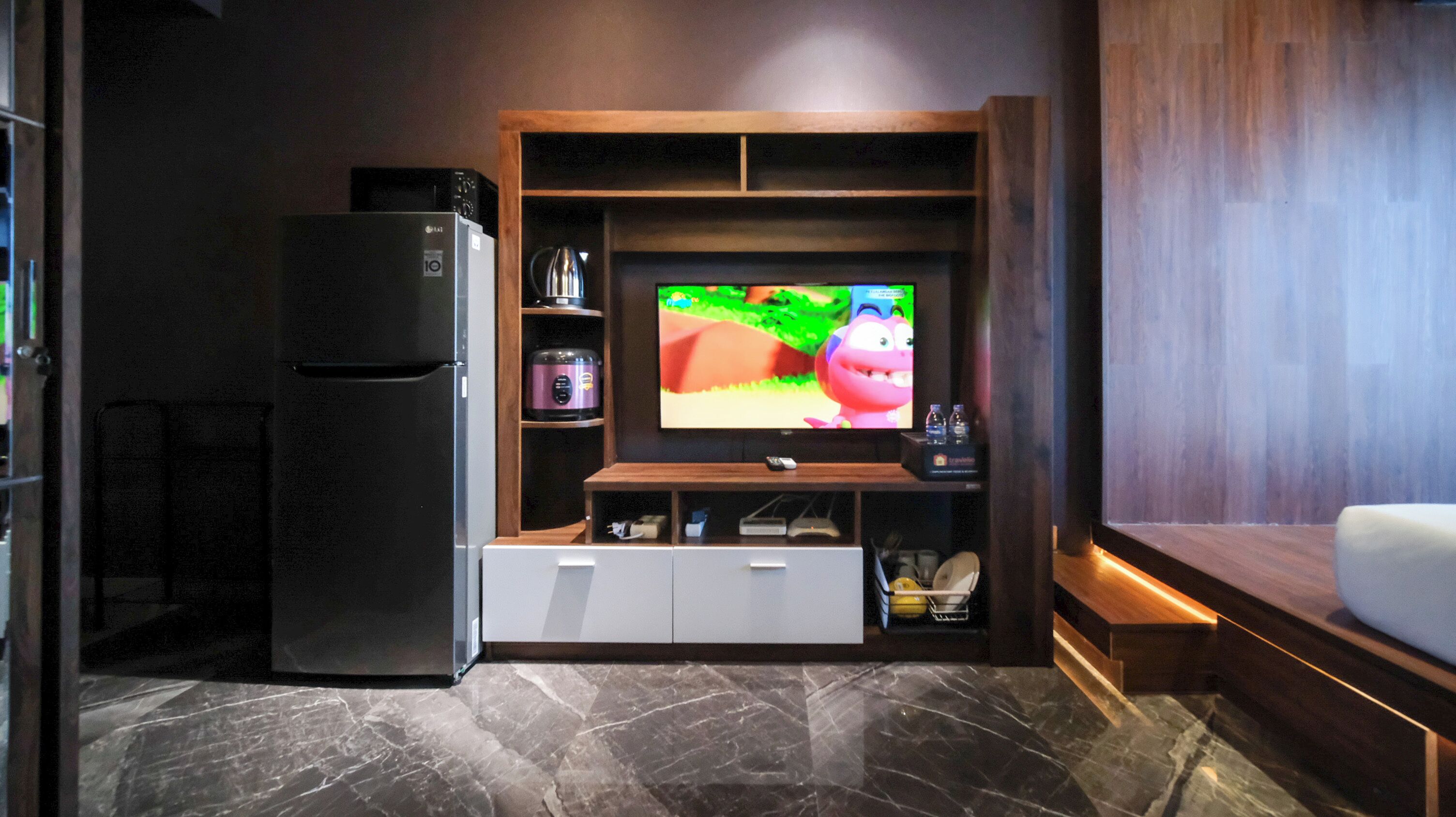 A modern living room with a built-in TV, a black refrigerator, and a wooden entertainment unit.
