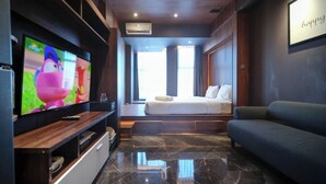 A modern hotel room with a large flat-screen TV, a bed with a view, a sofa, and a marble floor. - Simple And Modern Studio (No Kitchen) Anderson Supermall Mansion Apartment (Surabaya)