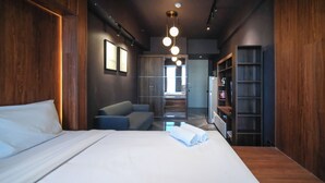 A modern hotel room with a large bed, a seating area, a wardrobe, and a view into a bathroom. - Simple And Modern Studio (No Kitchen) Anderson Supermall Mansion Apartment (Surabaya)