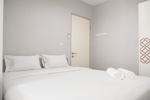 A hotel room with a bed, white linens, a door, and a towel on the bed. - Cozy Apartment With 2Br At M-Town Residence (Gading Serpong)