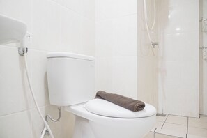 A white toilet with a brown towel on the seat, a white sink, and a shower area. - Cozy Apartment With 2Br At M-Town Residence (Gading Serpong)