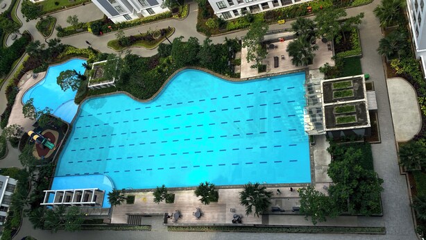 Vista aerea di una piscina circondata da un'area paesaggistica, con vialetti, posti a sedere e vegetazione.
