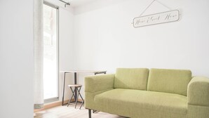 Una stanza con un divano verde, un tavolino e un cartello appeso al muro.