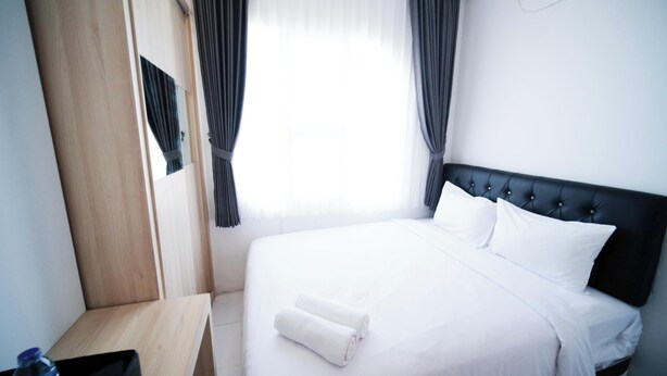 A hotel room with a bed, a wooden nightstand, a mirror, and a window with curtains. - Best Location And Restful 1Br At The City Square Apartment (Surabaya)