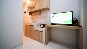 A modern kitchen with wooden cabinets, a built-in stove, and a flat-screen TV on a wooden shelf. - Best Location And Restful 1Br At The City Square Apartment (Surabaya)