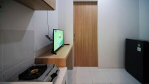 A small kitchenette with a gas stove, a television on a wooden shelf, and a door in the background. - Best Location And Restful 1Br At The City Square Apartment (Surabaya)