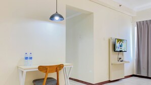 A room with a white desk, a wooden chair, a television on a stand, and a water bottle on the desk. - Modern Studio (No Kitchen) Grand Palace Kemayoran Apartment (Free Ipl & Utilities) (Jakarta)