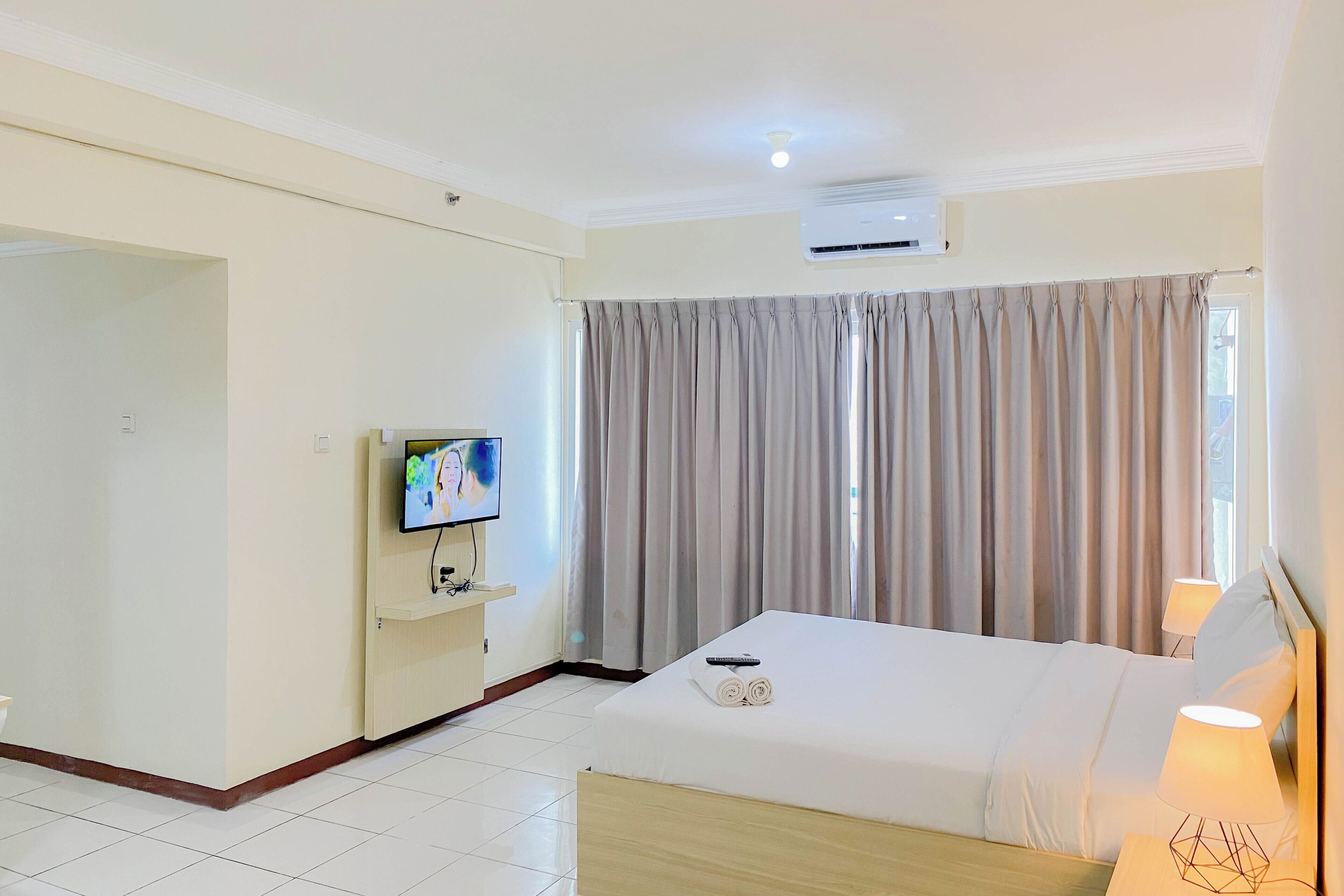 A hotel room with a bed, a TV, a desk, and a window with curtains.