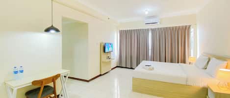 Habitación de hotel con cama, escritorio, silla, televisor y ventana con cortinas.