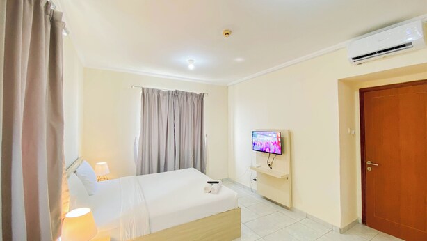 A hotel room with a bed, a TV, an air conditioner, and a door. - Restful Studio (Free Ipl & Utilities) Grand Palace Kemayoran Apartment (Jakarta)