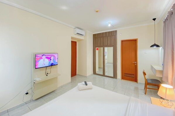 A hotel room with a bed, a TV on the wall, a desk with a chair, and a door leading to a bathroom.
