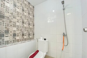 A bathroom with a geometric patterned wall, featuring a toilet, handheld showerhead, and towel.
