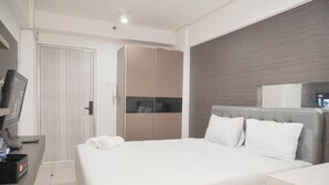 A modern hotel room with a large bed, a desk with a computer, a wardrobe, and a television. - Cozy Living Studio At Green Bay Pluit Apartment (Jakarta)