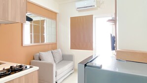 A modern kitchen with a built-in stove, a grey sofa, and a large window with blinds. - Comfort Designed 2Br Green Pramuka City Apartment (Jakarta)
