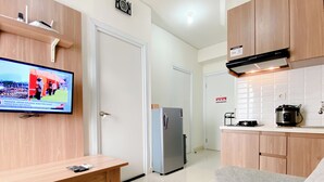 A modern kitchen with a refrigerator, stove, and a microwave. There is a wooden bench and a grey sofa in the living area. - Comfort Designed 2Br Green Pramuka City Apartment (Jakarta)
