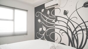 Una habitación de hotel con un ventanal grande, una cama con ropa blanca y un mural floral.