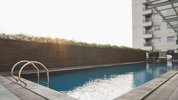 Una piscina con escaleras de metal, un deck de concreto y un edificio alto al fondo.