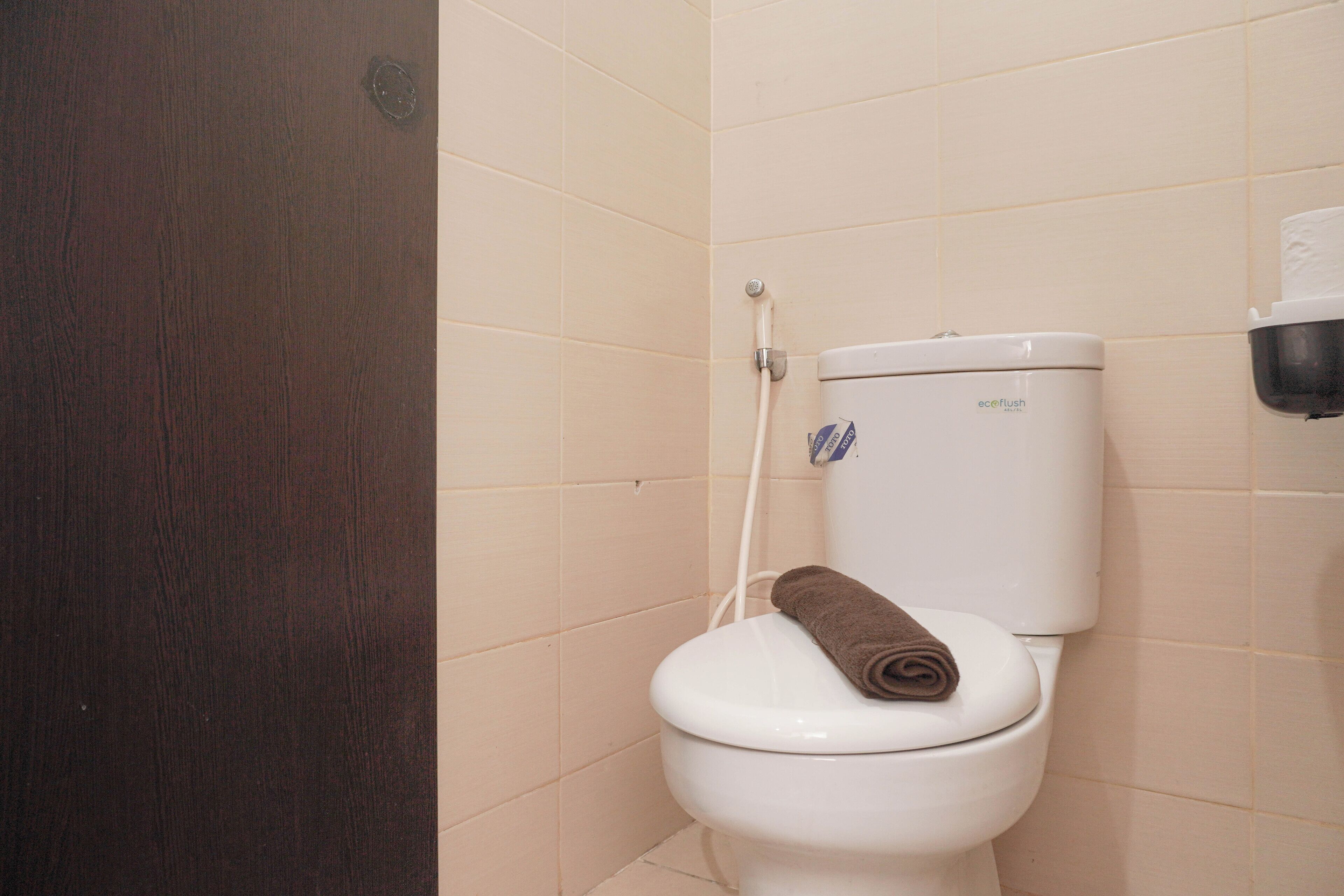 Een wit toilet met een bruine handdoek op de bril, een spoelhendel en een toiletrolhouder aan de muur.