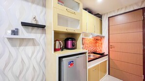 A compact kitchen with a refrigerator, a microwave, and a sink. There are wooden cabinets and a small shelf with a decorative item. - Good Place Studio Apartment At Vida View Makassar (Makassar)