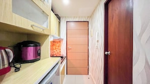 A narrow hallway with a wooden door, a shelf with a pink appliance, and a patterned wall. - Good Place Studio Apartment At Vida View Makassar (Makassar)