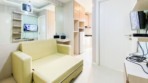 Un salon moderne comprenant un canapé, un téléviseur à écran plat fixé au mur, un coin cuisine avec des placards et une porte donnant sur une autre pièce.