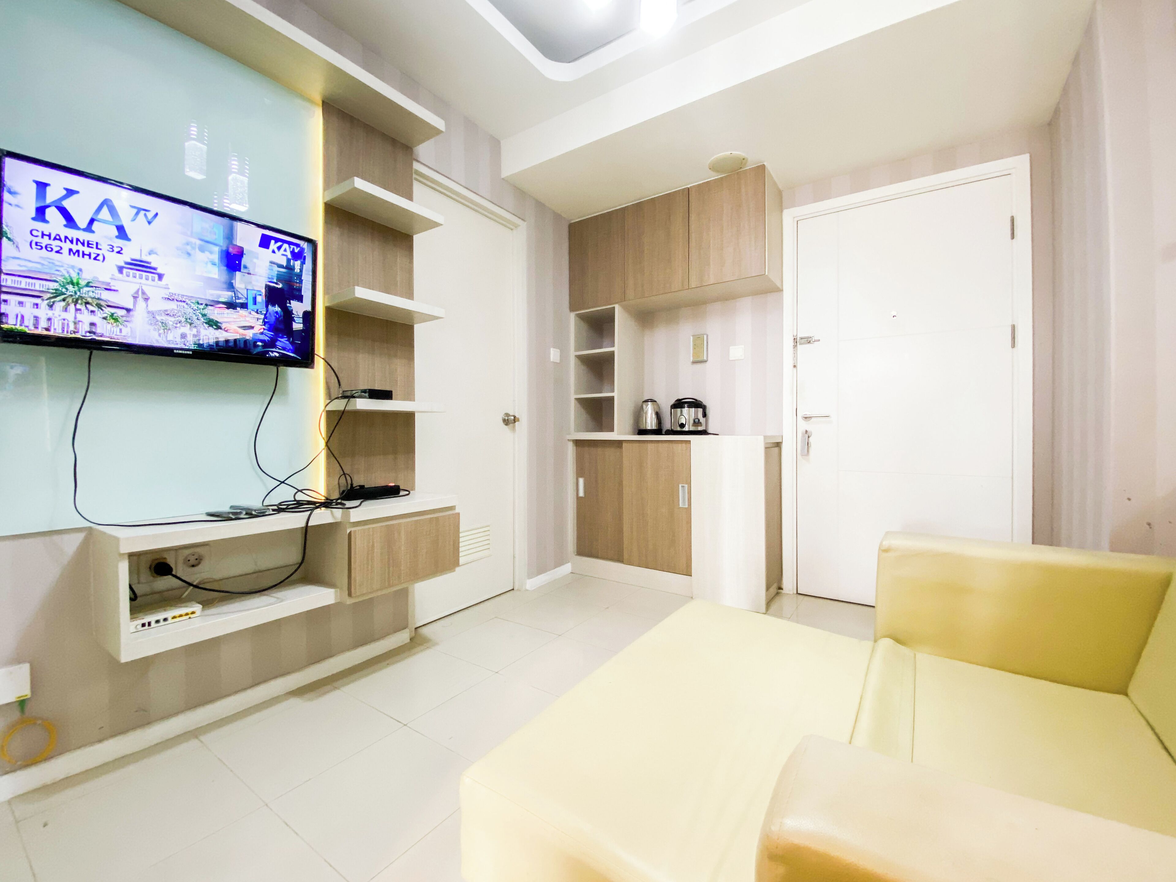A modern living room with a flat-screen TV mounted on the wall, a sofa, and built-in shelves with a kettle and other items.