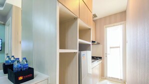 Une cuisine de taille réduite, équipée d’un réfrigérateur, d’un plan de travail avec des bouteilles d’eau, et d’une porte donnant sur une autre pièce.
