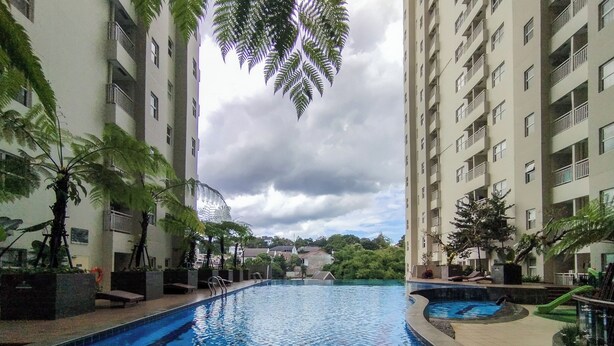 Une piscine entourée de grands immeubles d’habitation, avec des palmiers et un ciel nuageux.