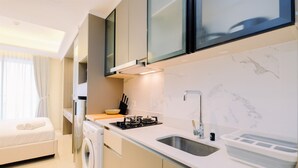 A compact kitchen with a built-in washing machine, a sink, and a stove. - Modern Look And Comfy Studio Gold Coast Apartment (Jakarta)