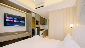 A hotel room with a bed, a TV mounted on the wall, a washing machine, and a small kitchenette. - Modern Look And Comfy Studio Gold Coast Apartment (Jakarta)