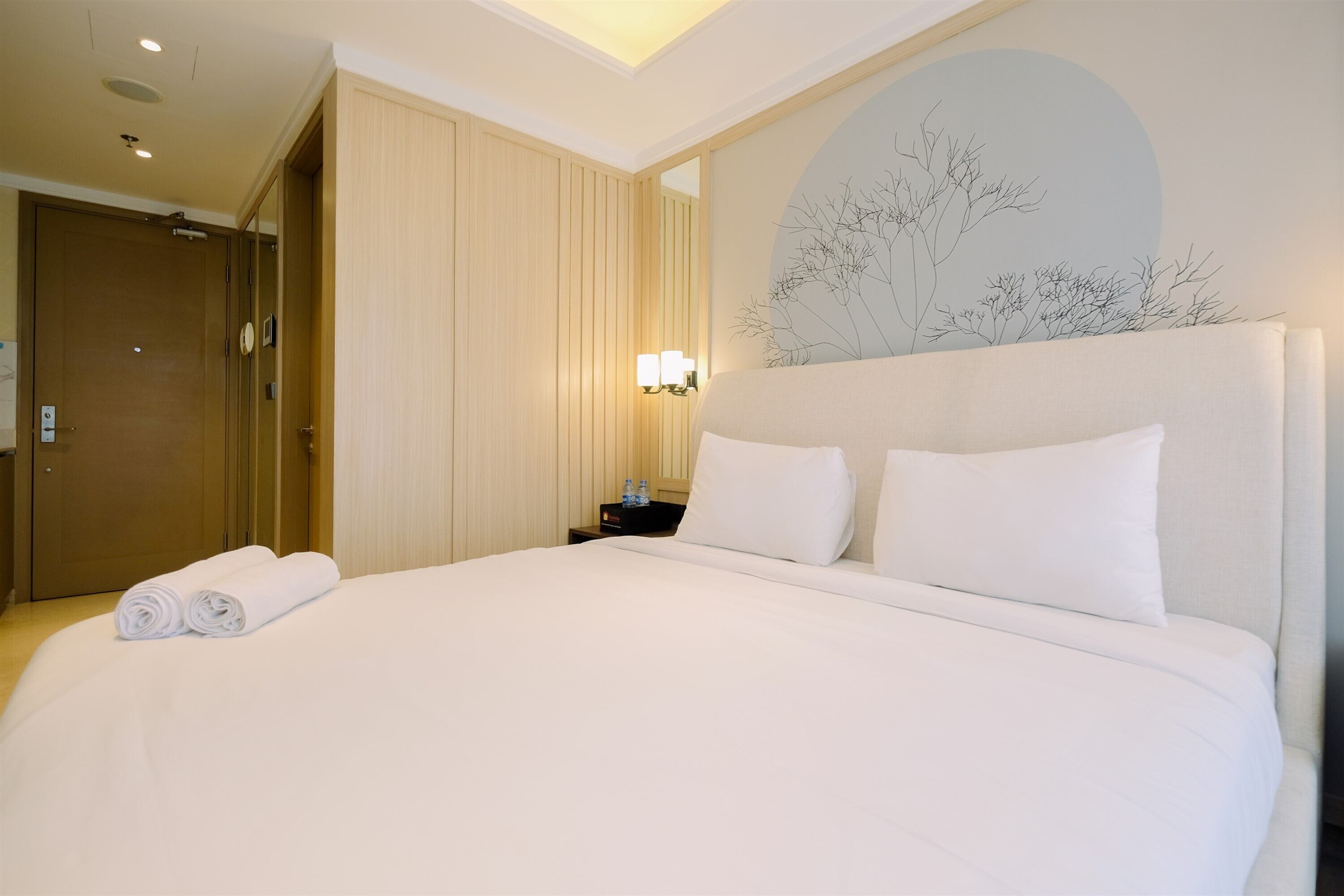 Una cama grande con ropa blanca, una mesita de noche con lámpara y una obra de arte colgada en la pared.