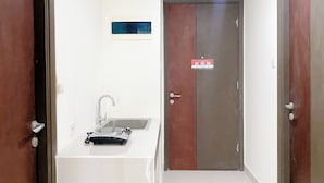 A narrow hallway with a sink and mirror on one side, a door with a red and brown panel, and a small blue sign on the wall. - Well Furnished And Cozy 2Br Pollux Chadstone Apartment (Cikarang)