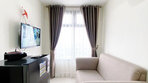 A hotel room with a black reception desk, a beige sofa, and a window with striped curtains. - Well Furnished And Cozy 2Br Pollux Chadstone Apartment (Cikarang)
