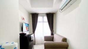 A small living room with a sofa, a TV, a small table, and an air conditioner. - Well Furnished And Cozy 2Br Pollux Chadstone Apartment (Cikarang)