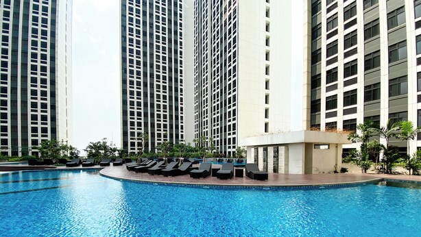A swimming pool with lounge chairs and tall buildings in the background. - Well Furnished And Cozy 2Br Pollux Chadstone Apartment (Cikarang)