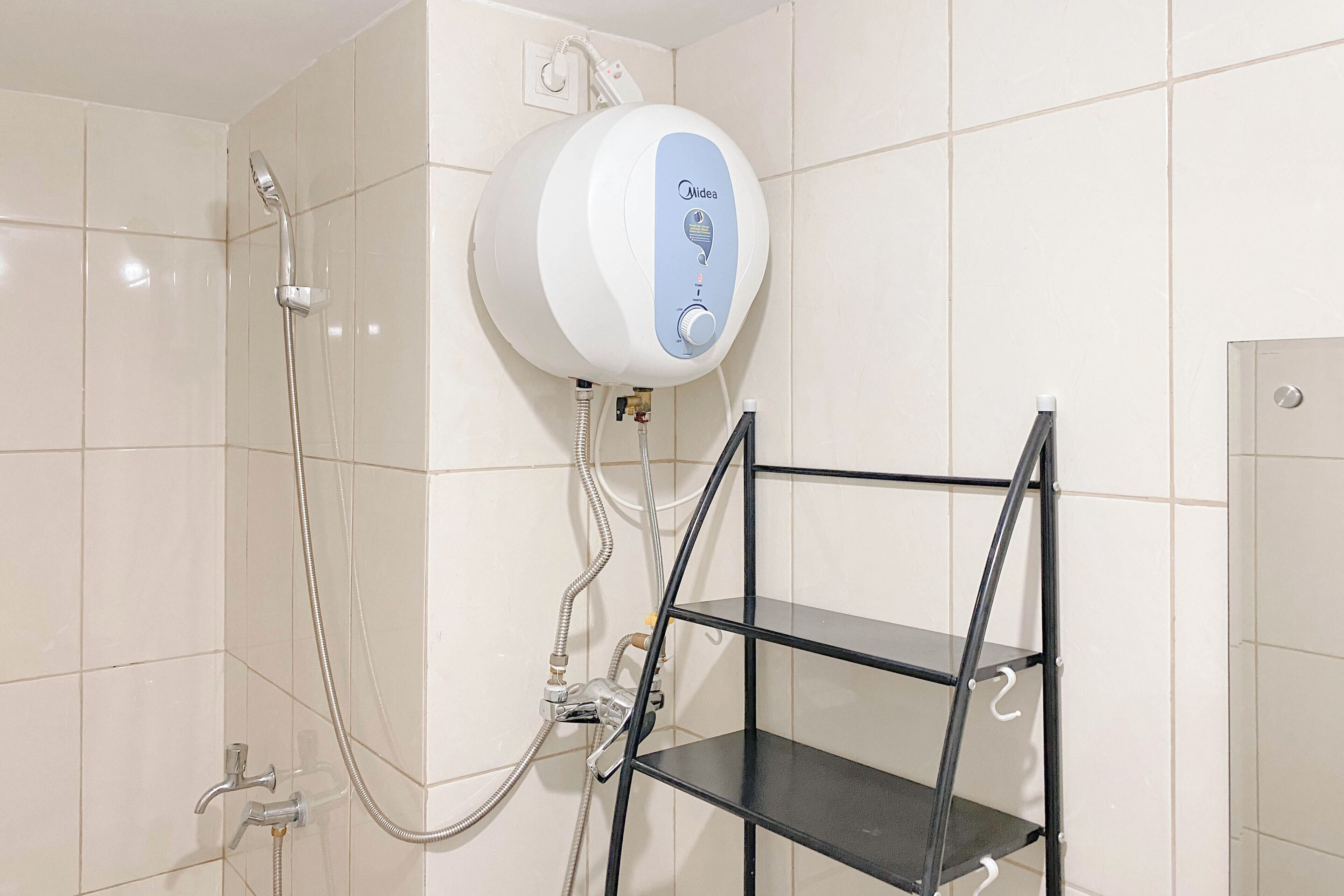 A bathroom with a wall-mounted water heater, a showerhead, and a black metal shelf unit.