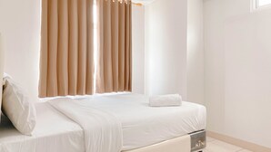 Ένα στρωμένο κρεβάτι με λευκά σεντόνια, μια μπεζ κουρτίνα και ένα μικρό παράθυρο με θέα προς τα έξω.