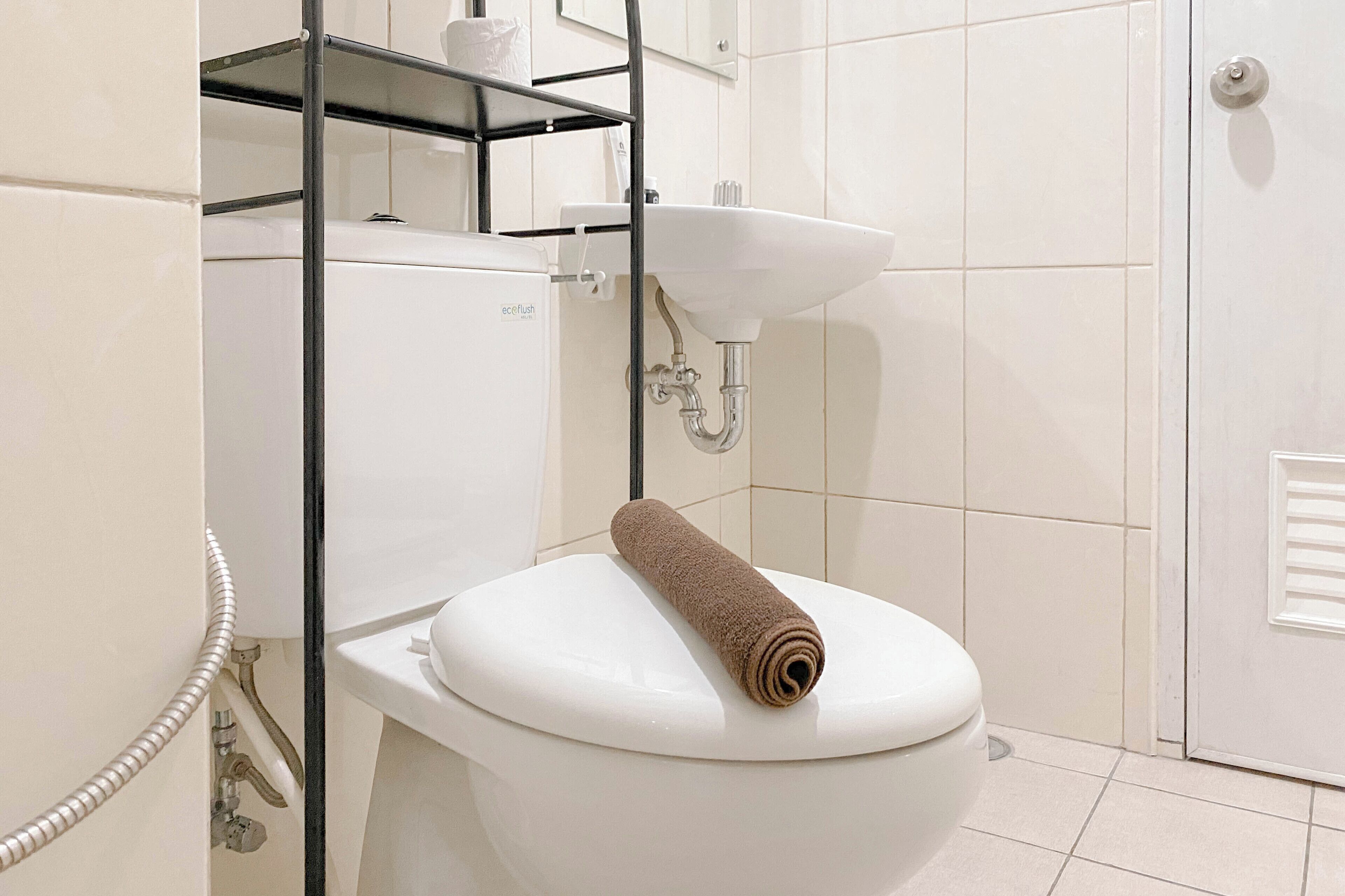 A white toilet with a towel on the seat, a white sink, and a metal shelf above the toilet.
