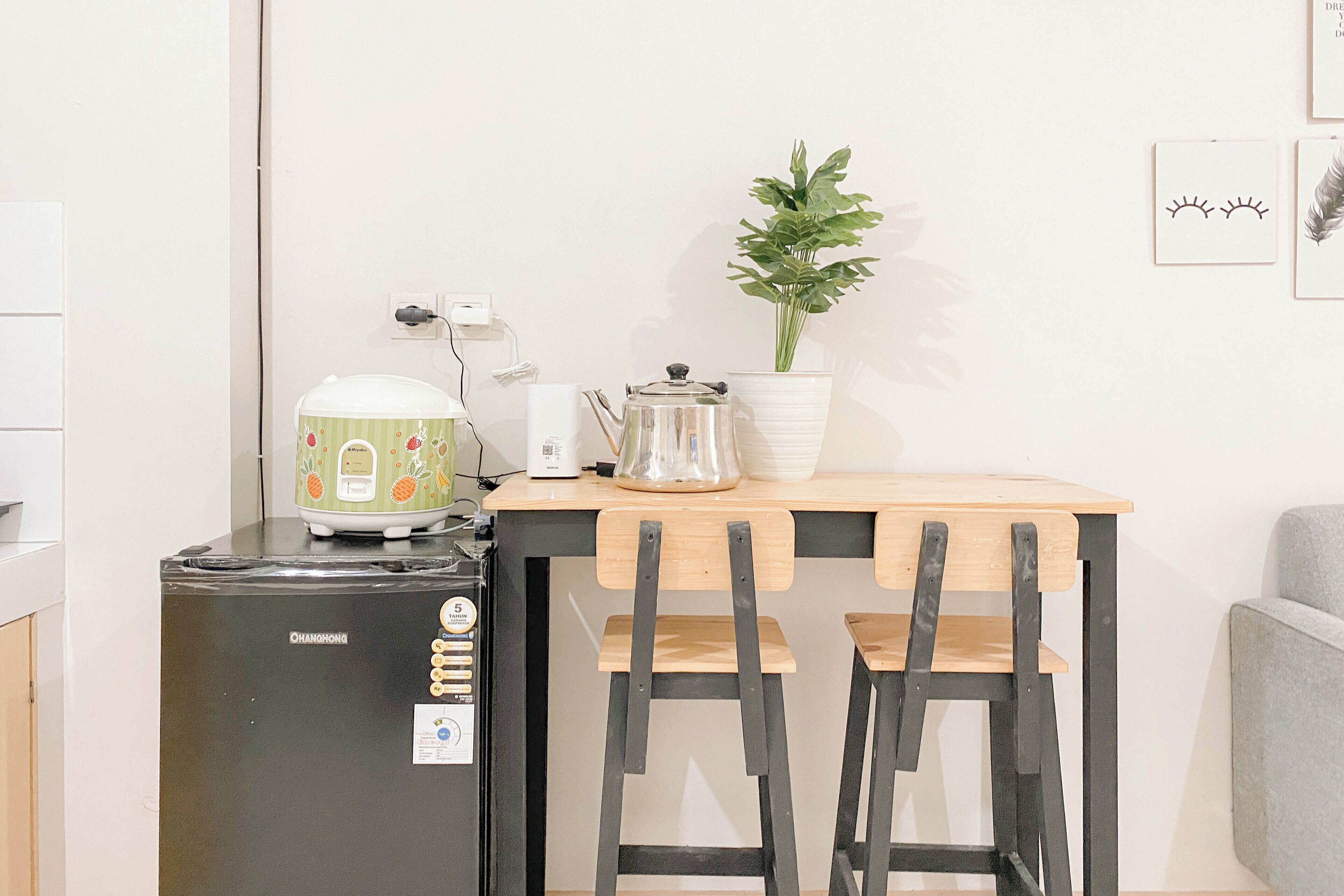 Une cuisine compacte équipée d’un réfrigérateur, d’une petite machine à café, d’une bouilloire et d’une plante en pot posée sur une table en bois.