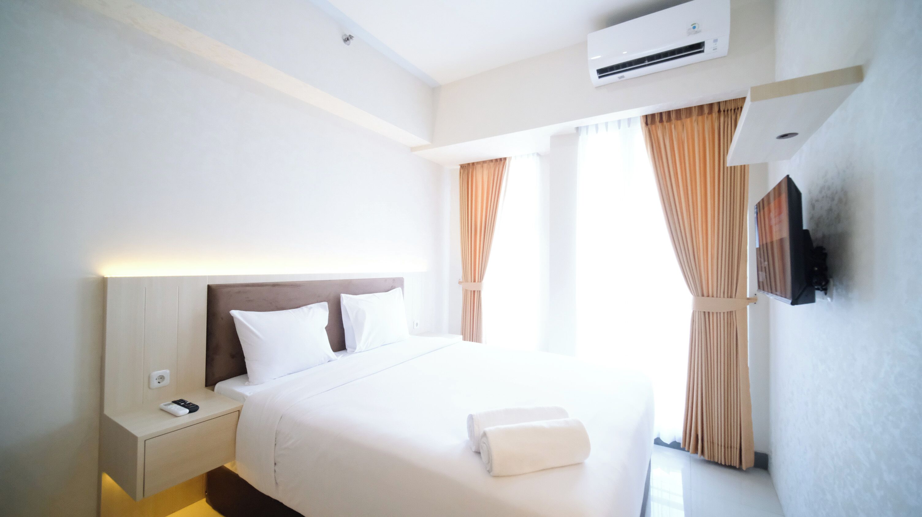 A hotel room with a bed, bedside table, and an air conditioning unit.