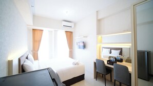 A hotel room with a bed, a desk with two chairs, a television, and an air conditioning unit. - Nice And Modern Studio At Benson Supermall Mansion Apartment (Surabaya)
