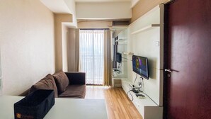 A modern living room with a sofa, a flat-screen TV mounted on the wall, and a sliding door leading to a balcony. - Signature 2Br At Apartment Tamansari Panoramic (Bandung)