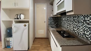 A compact kitchen with white cabinets, a refrigerator, a water dispenser, a microwave, a gas stove, and a tiled backsplash. - Signature 2Br At Apartment Tamansari Panoramic (Bandung)