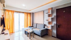 A modern living room with a grey sofa, a glass coffee table, and a wooden door. - Amazing 1Br Apartment Gateway Pasteur (Cimahi)