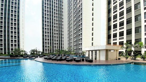 A swimming pool with lounge chairs and tall buildings in the background.