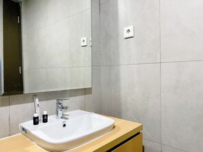 Un baño con lavamanos blanco, un espejo y dos botellas de artículos de aseo.